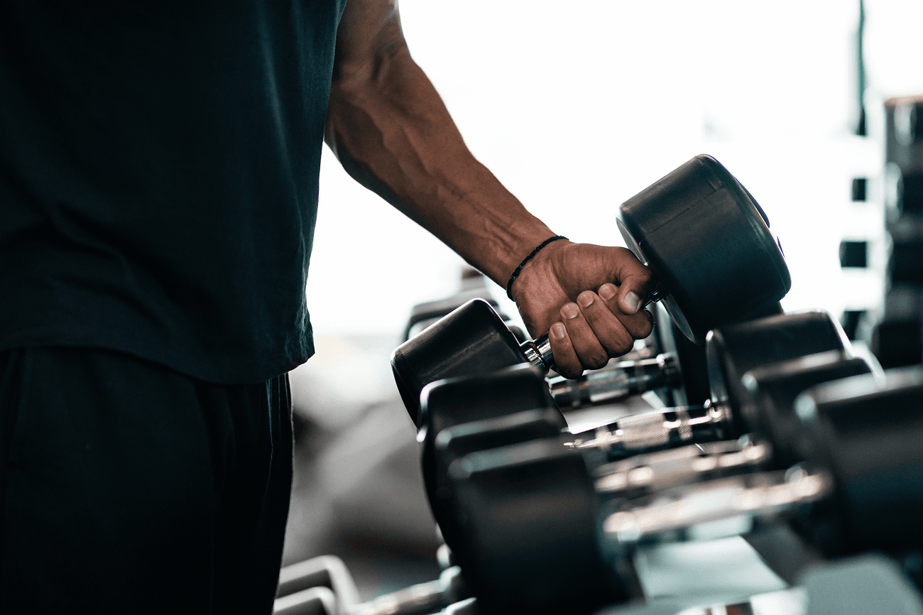 Close-up of a man holding a dumbbell beside a rack of weights in a gym.