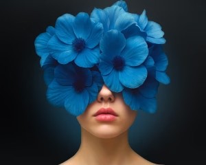 Spacious modern office with large windows, indoor plants, and people working at shared desks.