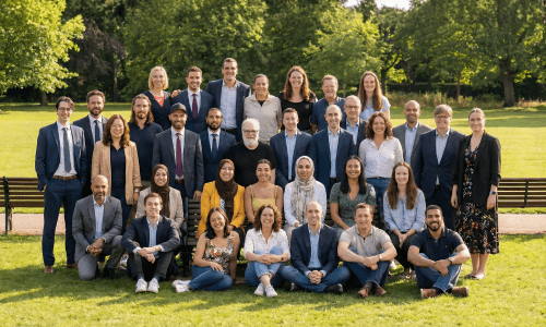 A large group photo of diverse team members gathered in an industrial-style space with arched ceiling.