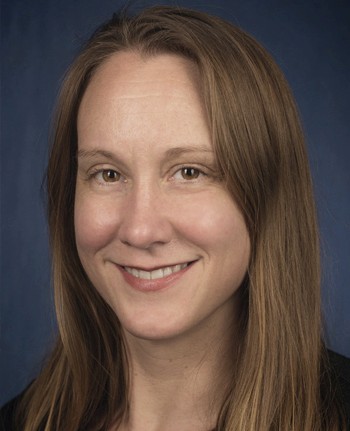 A smiling person with long brown hair, wearing a dark top, against a blue background.
