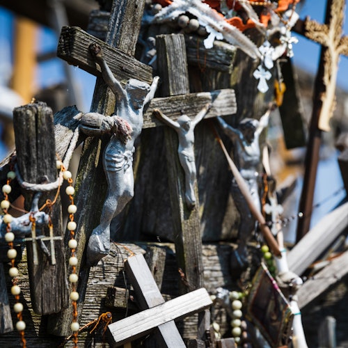 Various crucifixes and rosary beads are arranged on a wooden structure, with a clear blue sky in the background.