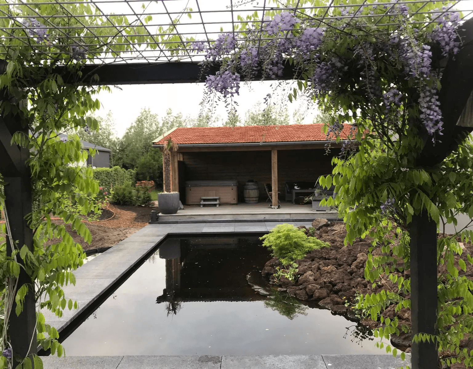 Moderne tuin met vijver, strakke bestrating en houten overkapping, voorbeeld van tuinaanleg in Gorredijk