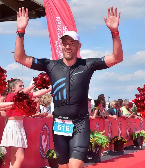 Izaak Quist steekt zijn handen omhoog bij de finishlijn van een triatlon, stralend na het voltooien van de race als 5 Day Fast-deelnemer.