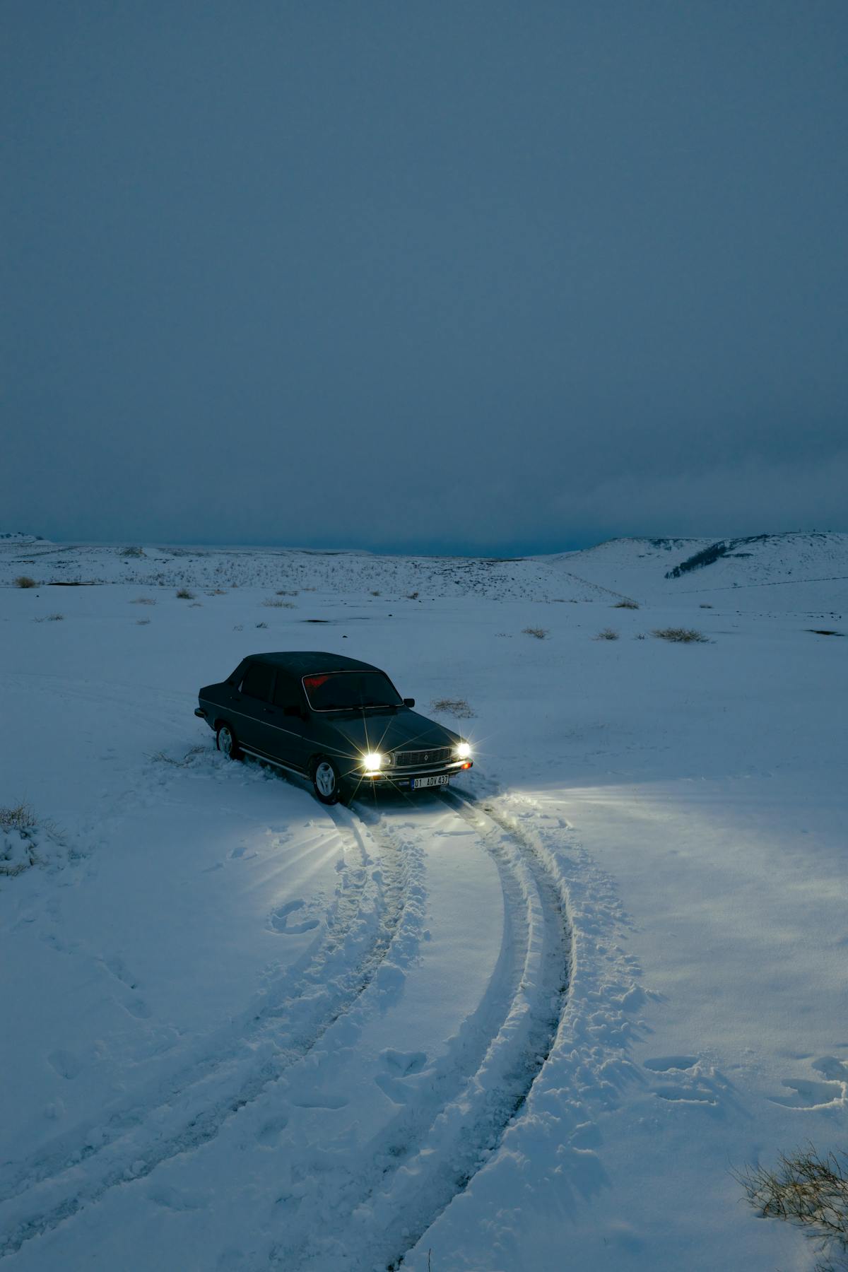 A lone car navigates through snow-covered terrain at twilight