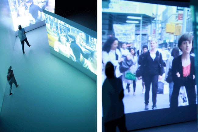 The image is a diptych, presenting two distinct scenes. On the left, a person stands with their back to the camera, observing two large screens mounted on a white wall. The screens display images of people in a city setting. On the right, a person stands facing the screens, which show a woman in a red shirt and a woman in a black jacket. The person on the right also holds a white bag. The lighting in the left scene is dim, giving it a darker ambiance. The right scene is brighter, with more ambient light.