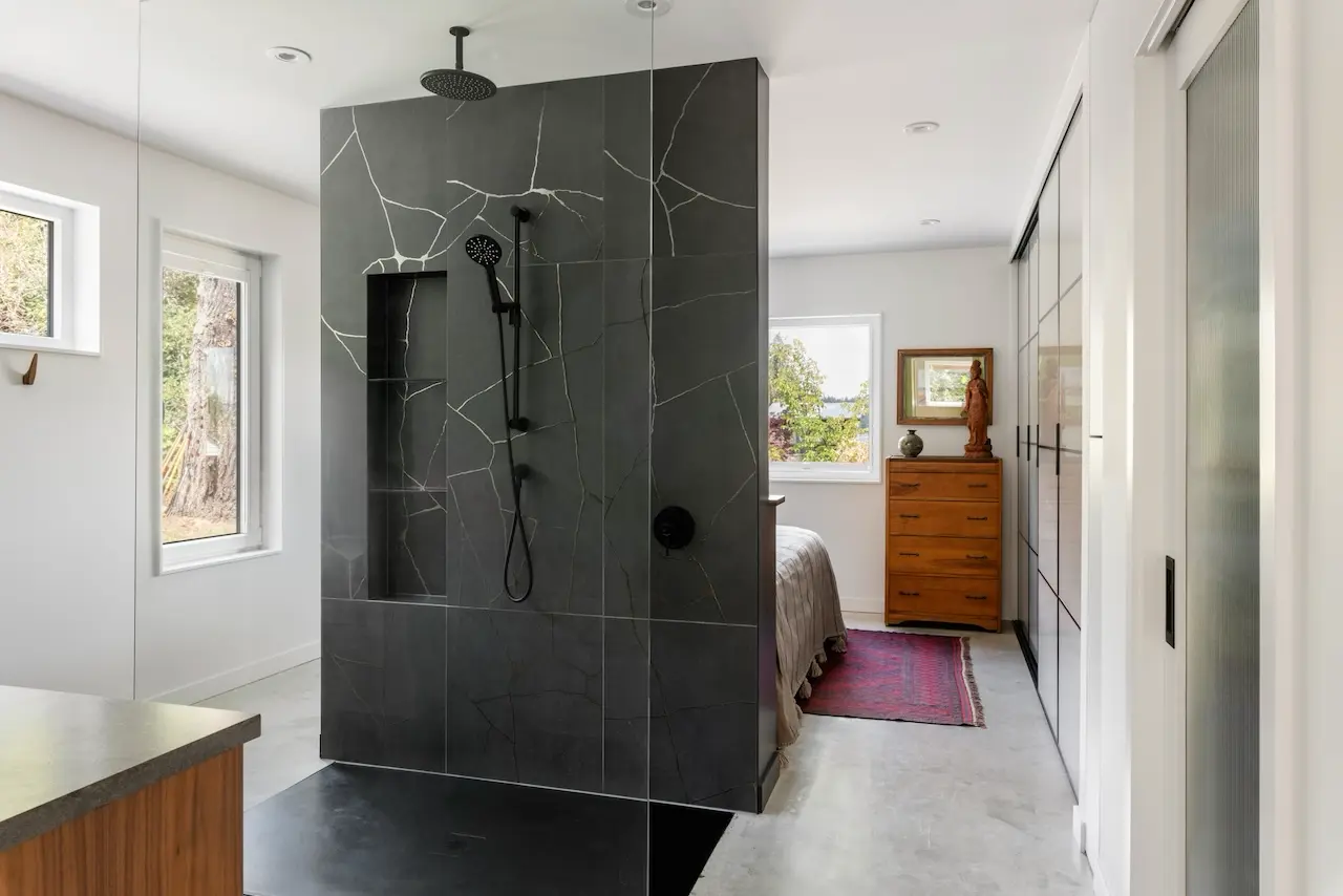 Modern two-story home with large glass windows, warmly lit interiors, and a balcony. Surrounded by trees and a manicured lawn at dusk. Cozy ambiance.