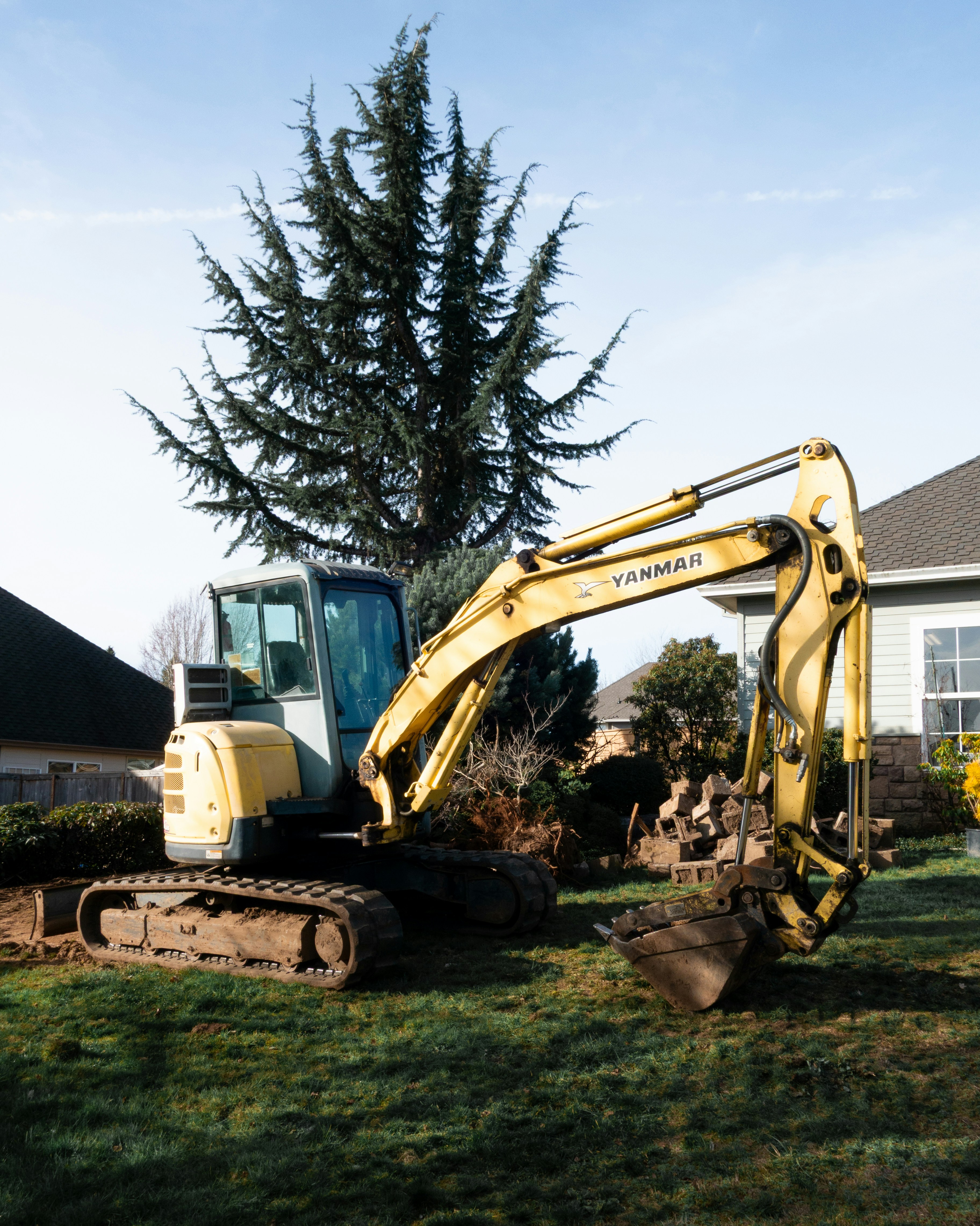 Yellow excavator digging in a residential backyard.