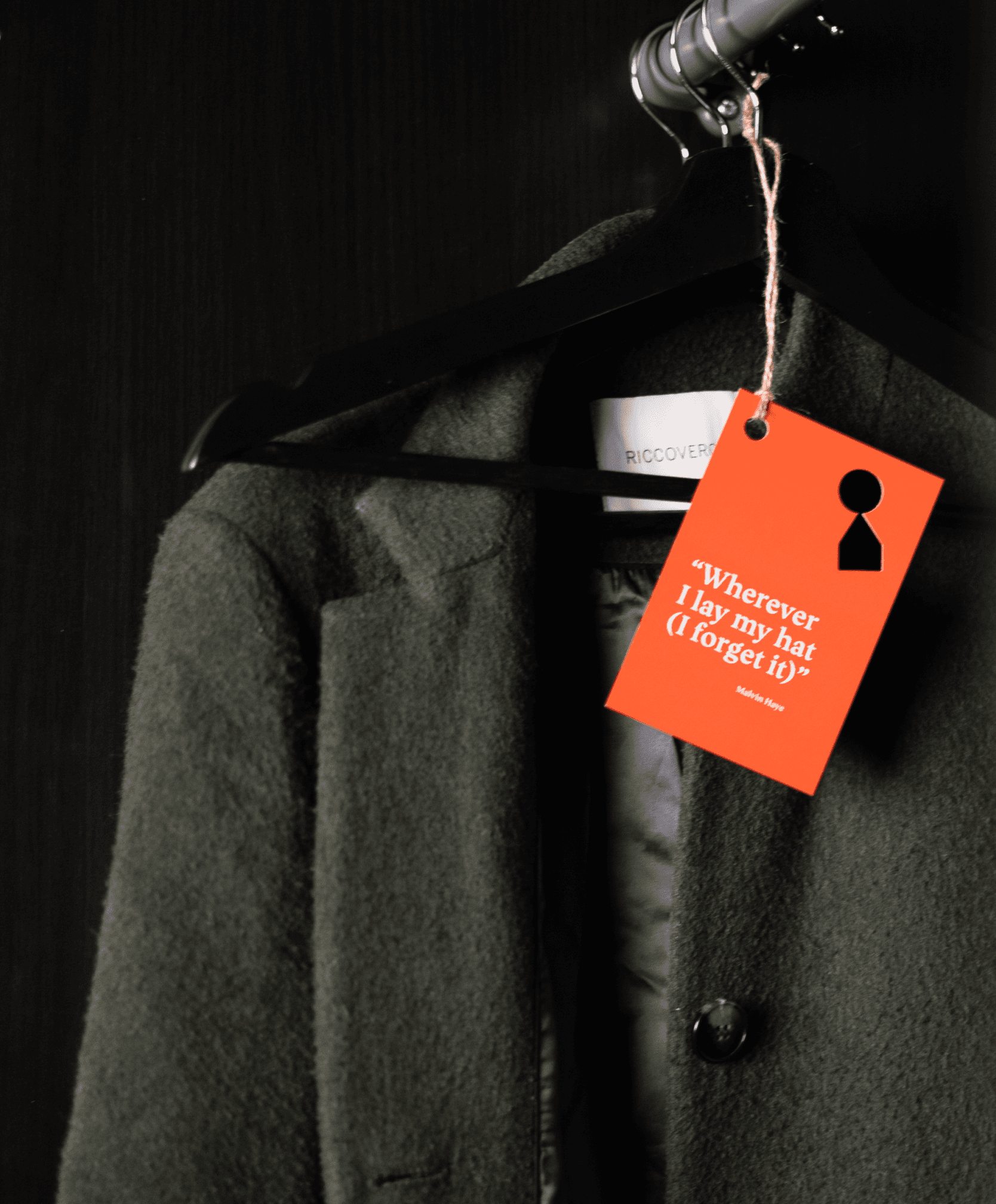 A wintercoat hanging in a closet with an orange tag attached to it with a keyhole punched out in the shape of the logo of Staysville and the text "Wherever I lay my hat (I forget it)".