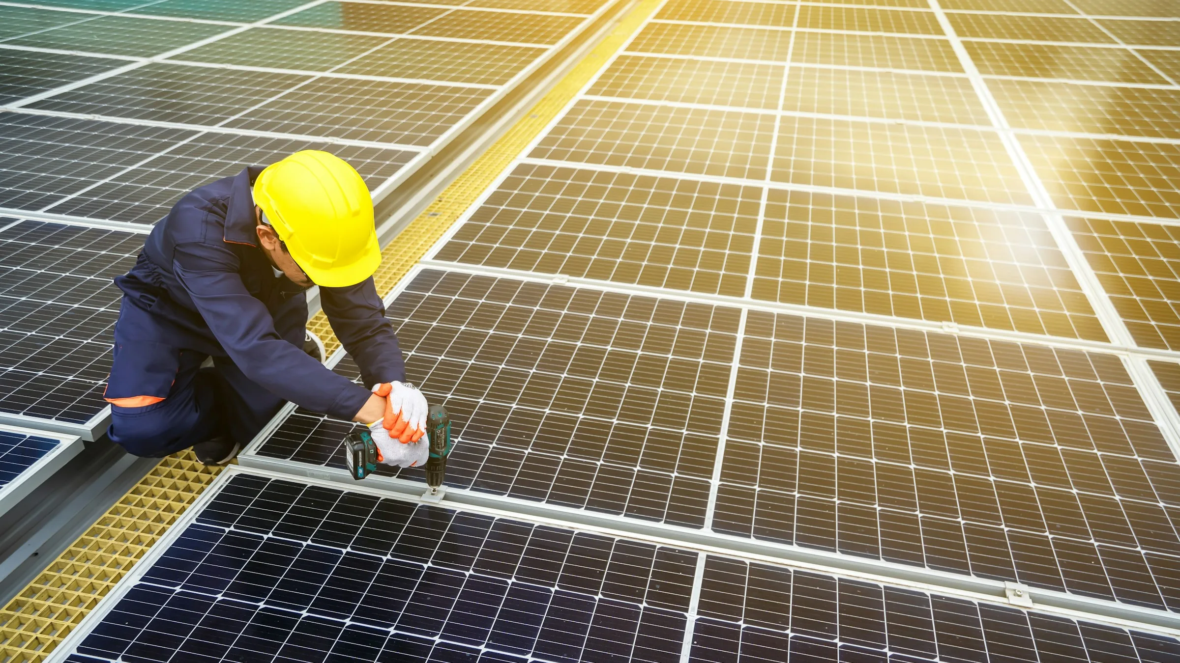 Technician in a yellow hard hat inspecting rows of solar panels on a sunny day