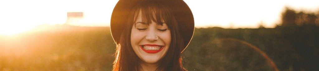 Woman in a hat smiling with eyes closed in sunny field.