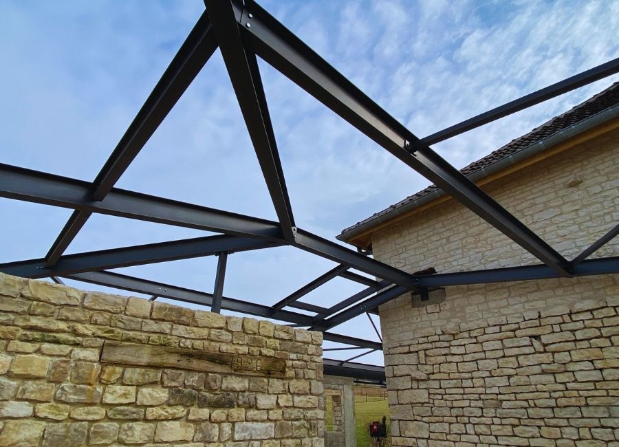 Structure métallique installée en toiture sur murs en pierre, vue depuis l’intérieur du bâtiment.
