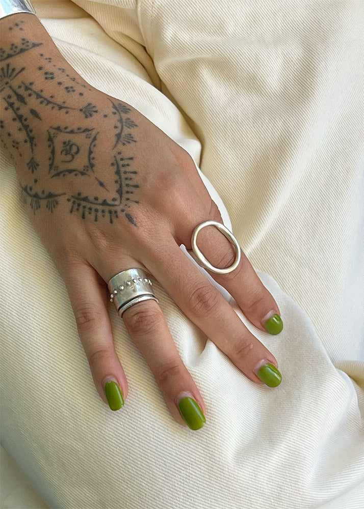 Hand with tattoos, green nail polish, and multiple rings on a light fabric background
