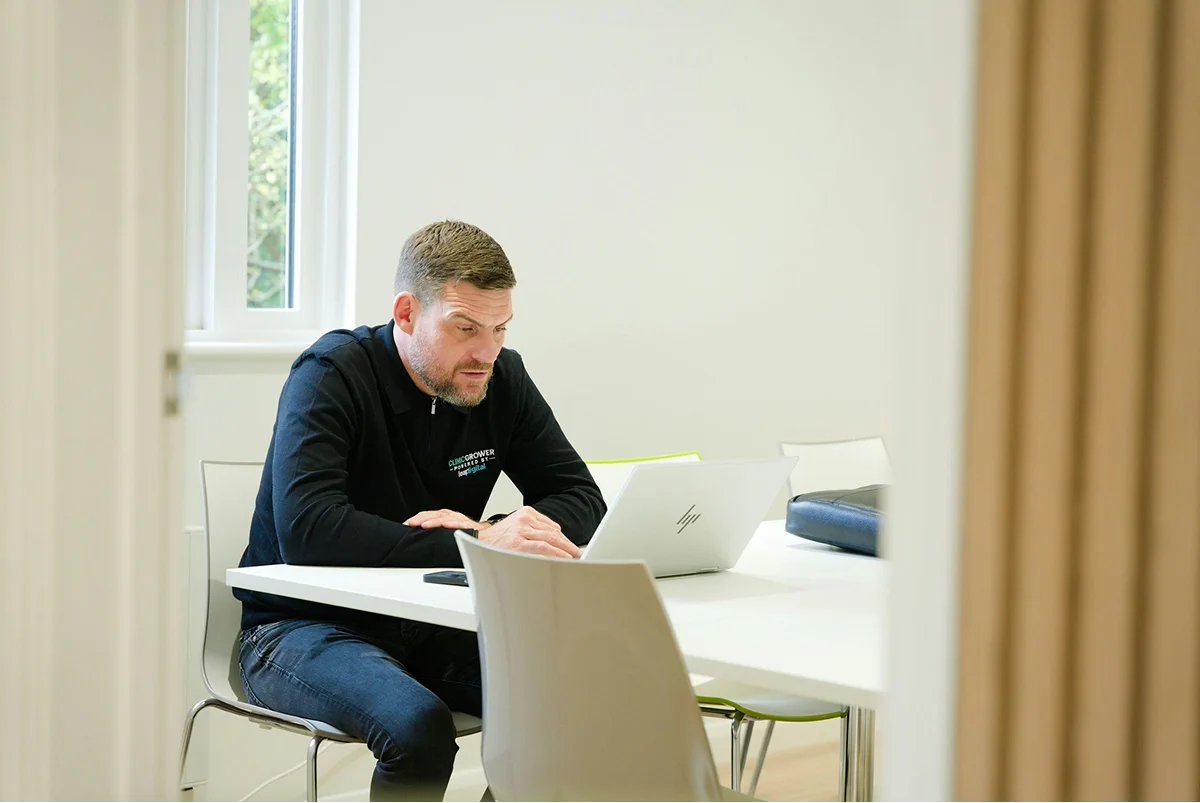 A man writing notes beside his laptop at a table.