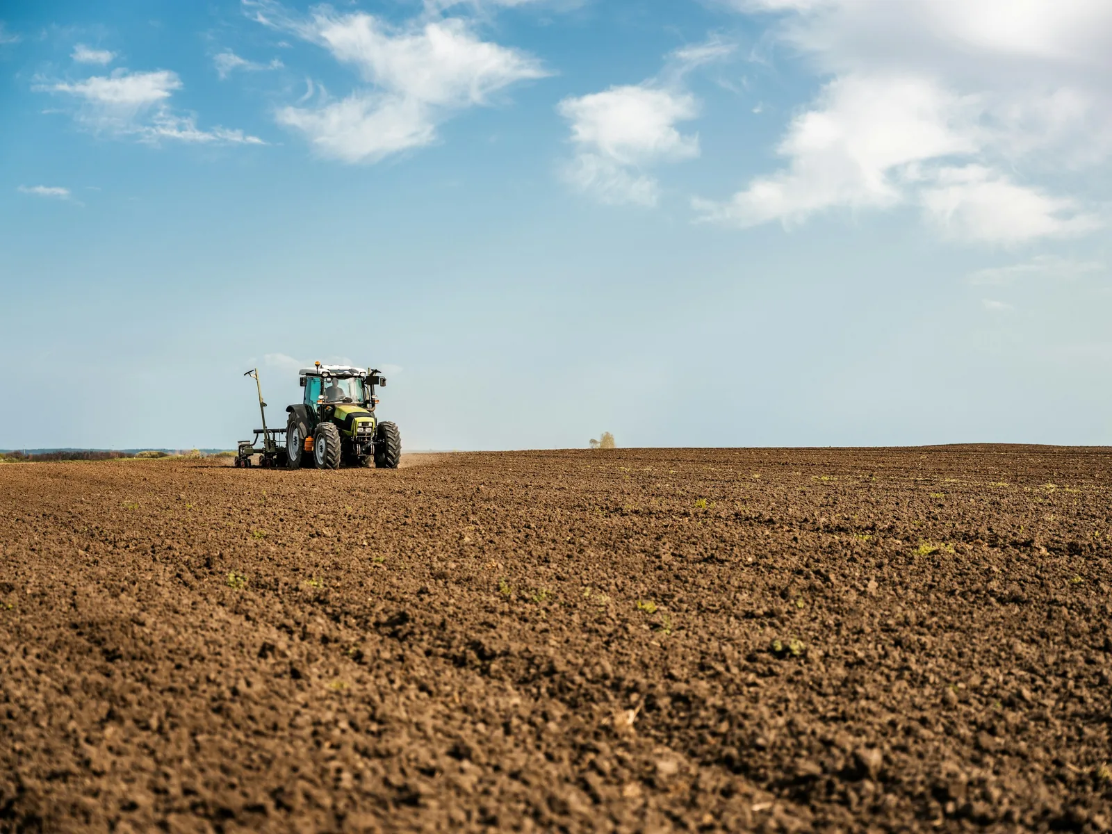 Traktor bei der Bodenbearbeitung auf einem Feld unter weitem Himmel