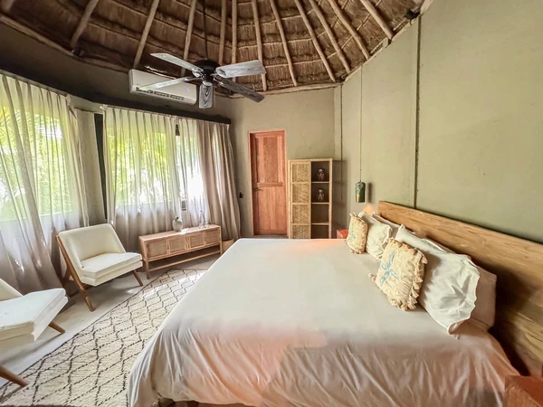 Villa de dos habitaciones con alberca en Nômade Tulum resaltando una cama grande con almohadas, ventilador de techo, silla y muebles decorativos.