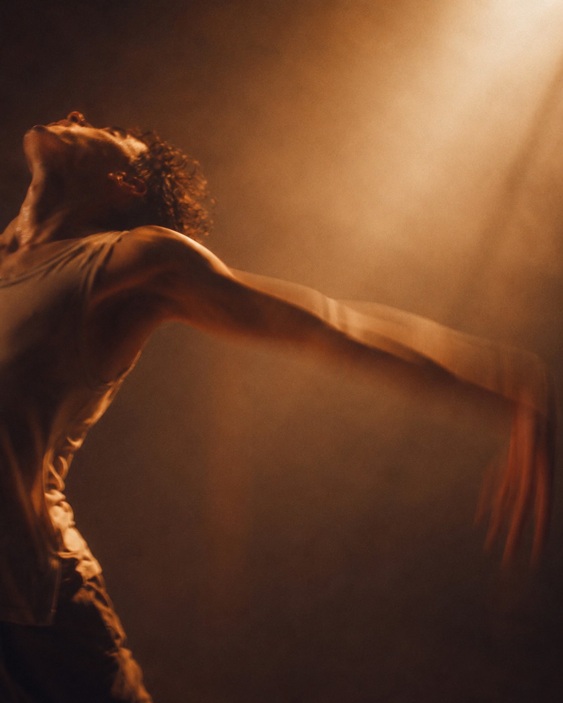 The close framing and motion blur transform the dancer’s gesture into pure energy, capturing a fleeting instant where movement outpaces form. Bathed in golden light, the figure appears to dissolve into the atmosphere itself, embodying both vulnerability and transcendence.