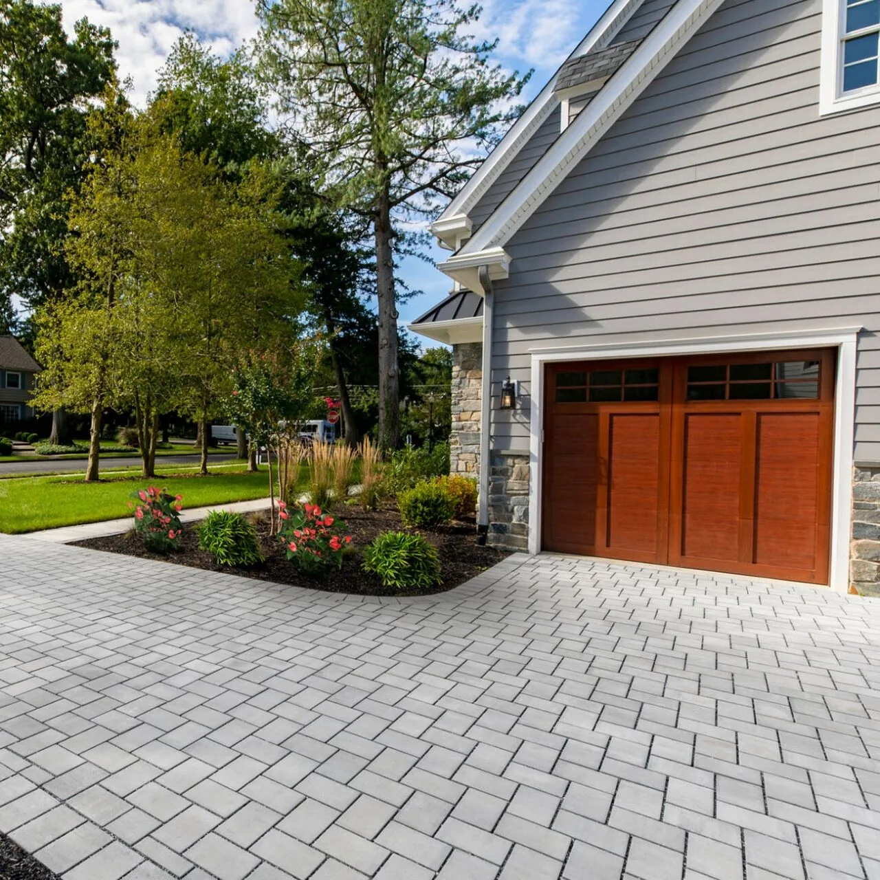 Light gray interlocking paver driveway beside a gray house with a wooden garage door.