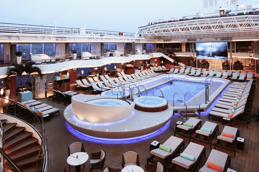 A sparkling blue swimming pool on the deck of a Holland America Line cruise ship, surrounded by empty lounge chairs under a clear sky.