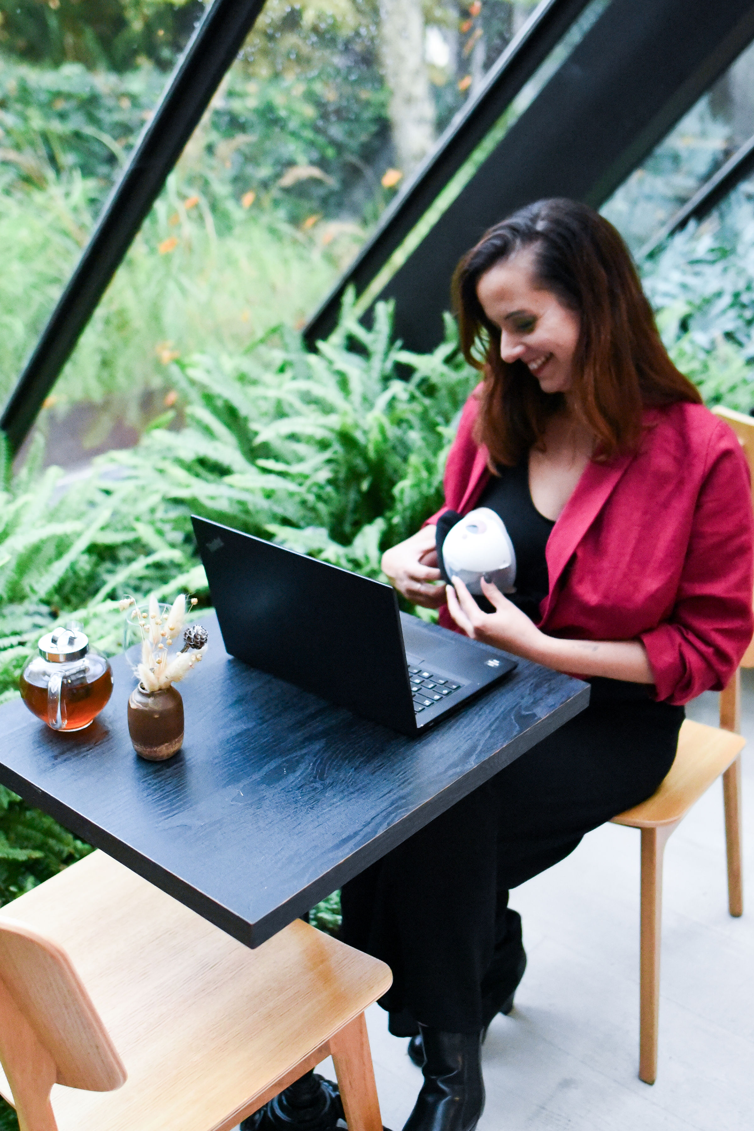 Femme assise à un bureau devant un ordinateur, portant un chemisier d’allaitement rouge framboise, illustrant l’utilisation du vêtement dans un contexte quotidien, pratique et élégant.