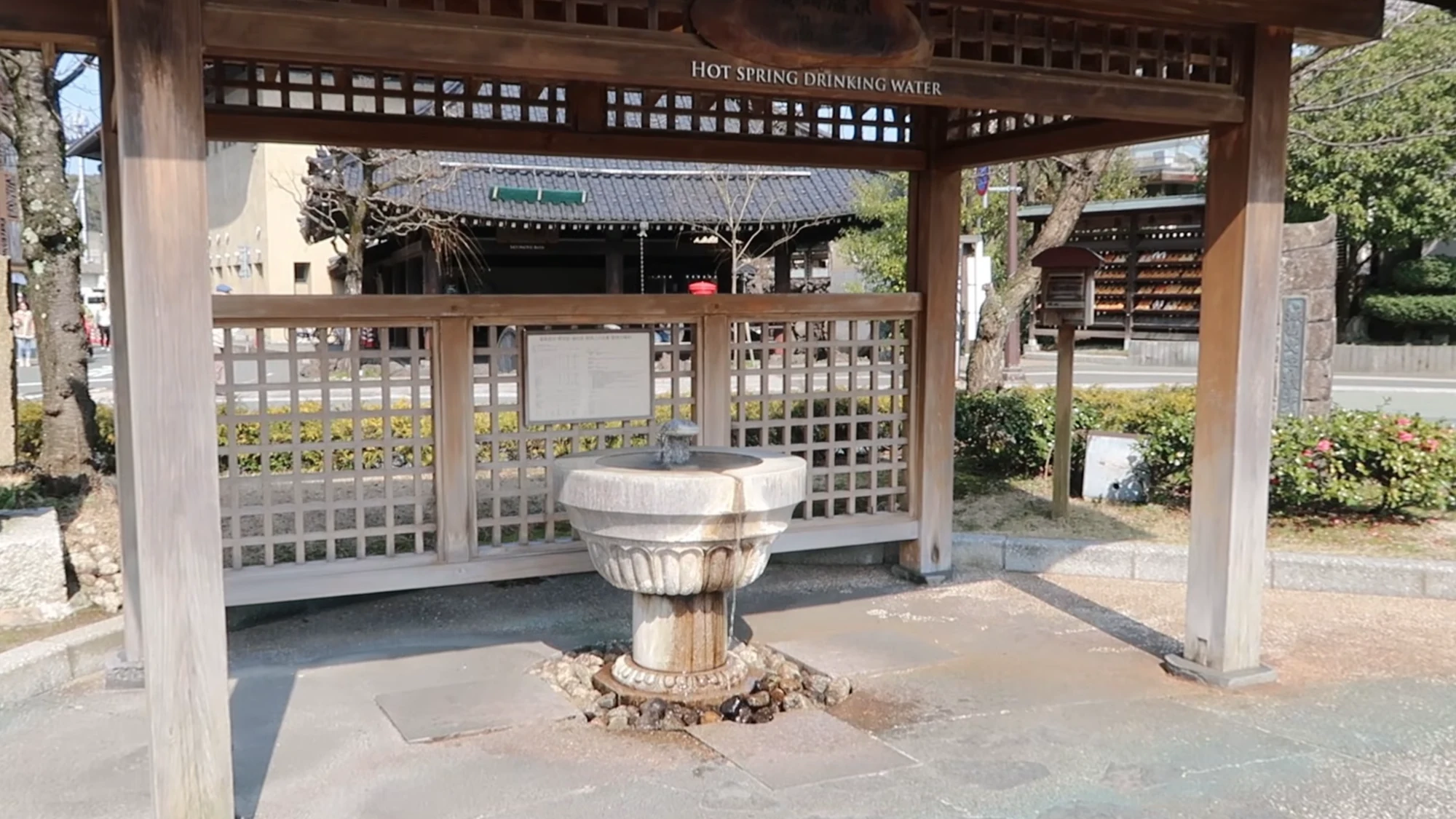 The hot spring drinking pavilion in Kinosaki seen from the street, twin basins under a tiled roof.