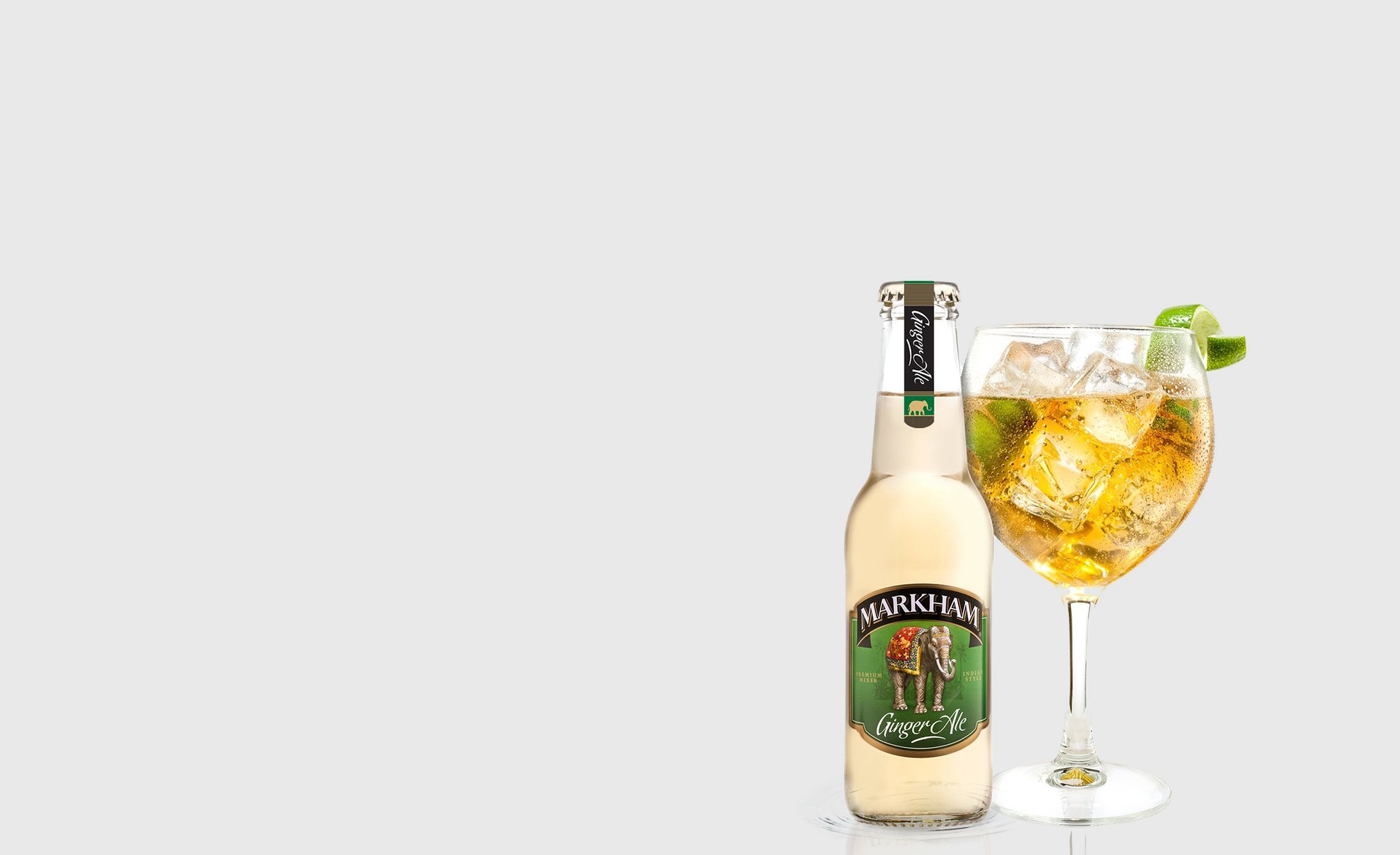 Bottle of ginger ale labeled "MARKHAM" next to a glass filled with iced drink and lime wedges. Both items are set against a plain gray background. Refreshing and crisp.