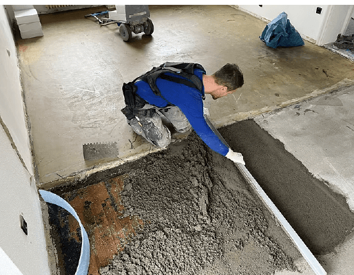 Ceramic installer using a lumbar support exoskeleton while preparing a floor on a construction site.