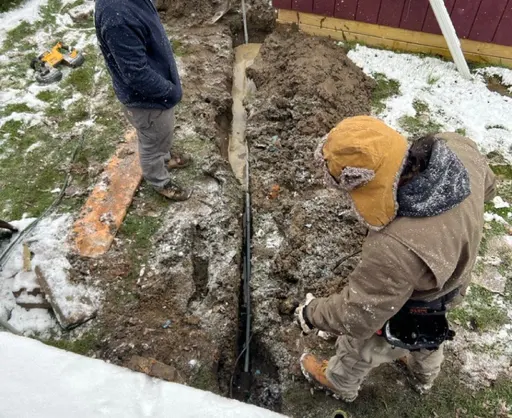 Workers digging a trench through snowy ground for underground electrical conduit installation.