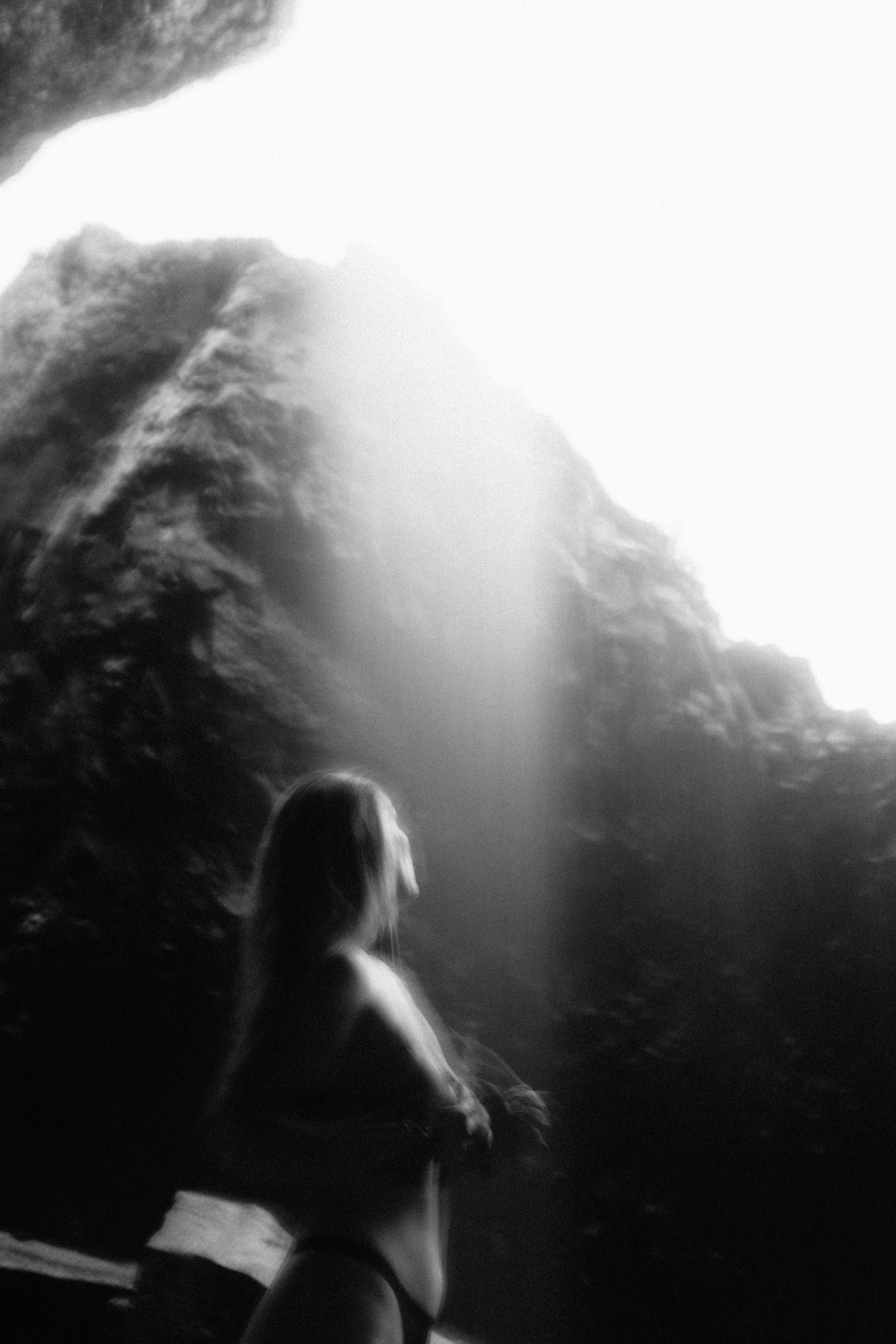 Woman stands below a waterfall in a cave.
