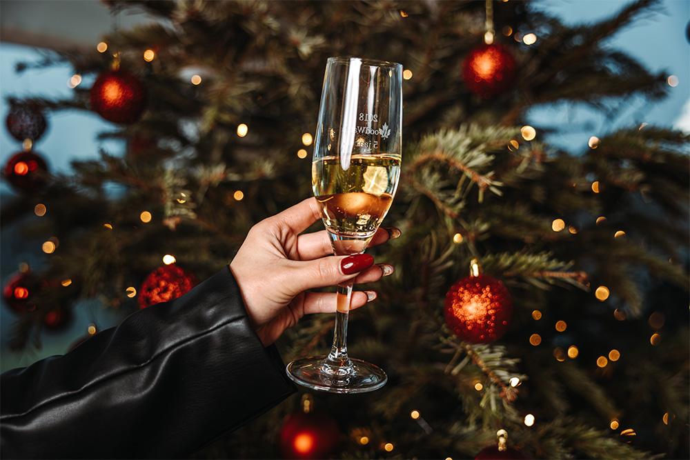 Personne tenant une flûte de champagne devant un arbre de Noël décoré