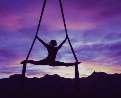 silouette of a woman doing the splits while hanging from silks on a sunset background