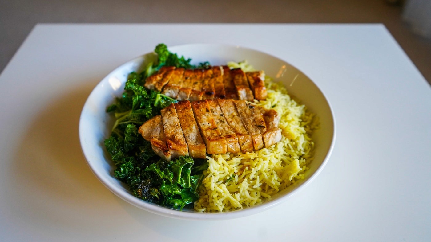 Sliced grilled chicken served over rice with sautéed greens, an easy way to anchor a smaller meal around protein.