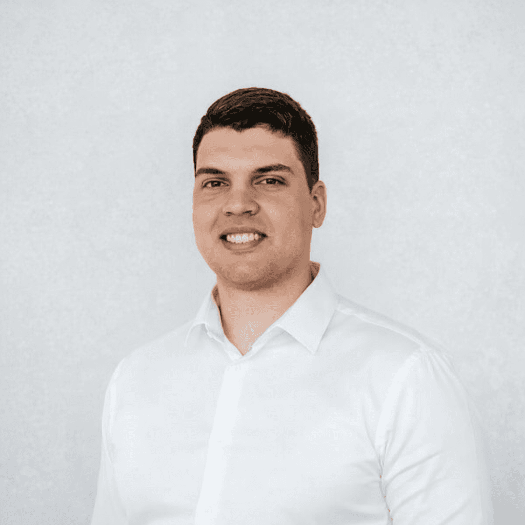 Smiling blonde woman with freckles in a white shirt, arms crossed, minimalist studio portrait.