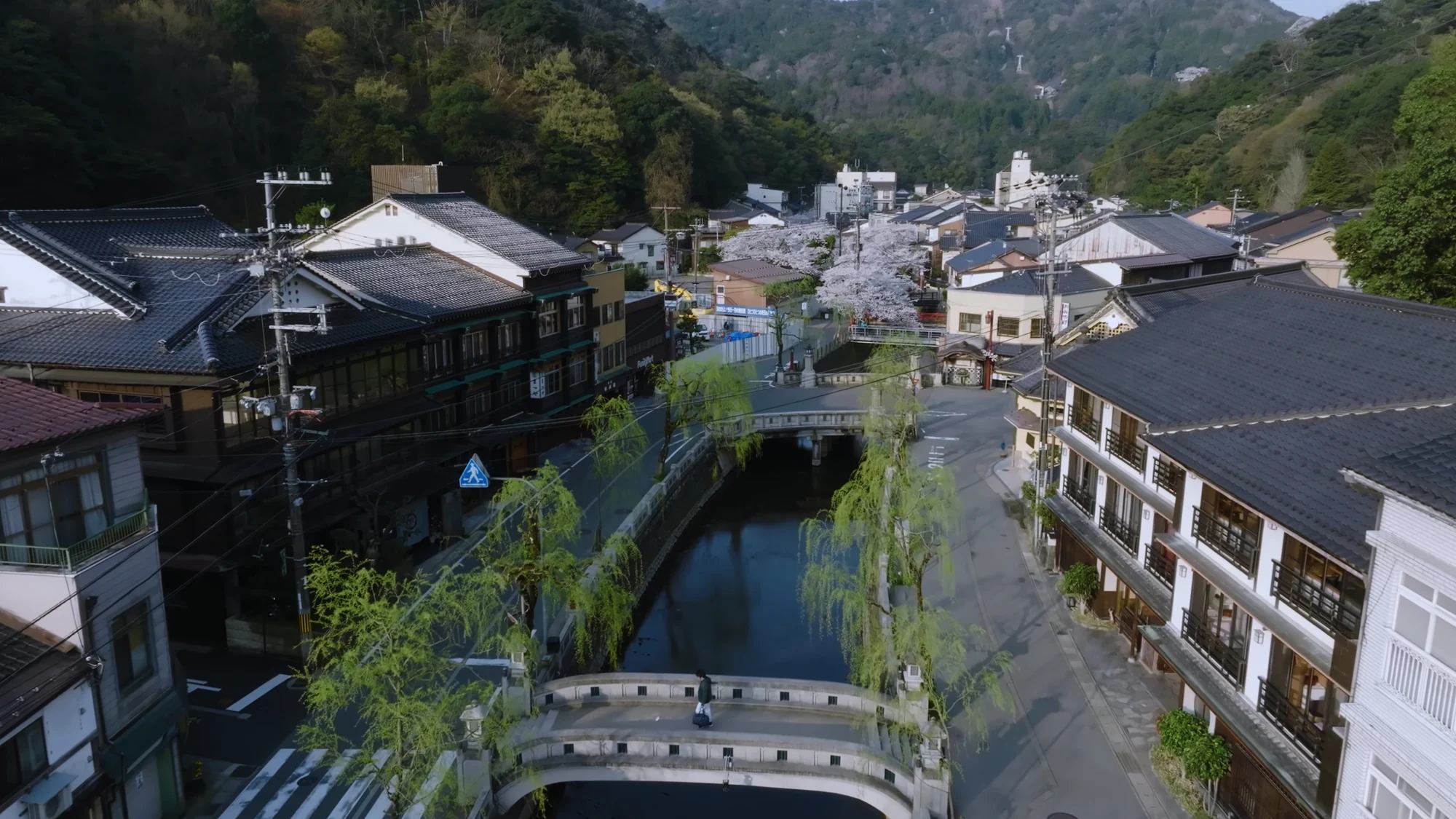 The Kinosaki canal seen from above in spring with budding willows along the stone embankment.