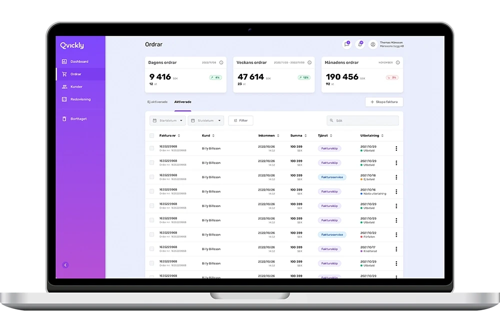 A young person with curly hair smiles at the camera while sitting in front of a laptop against a dark background.