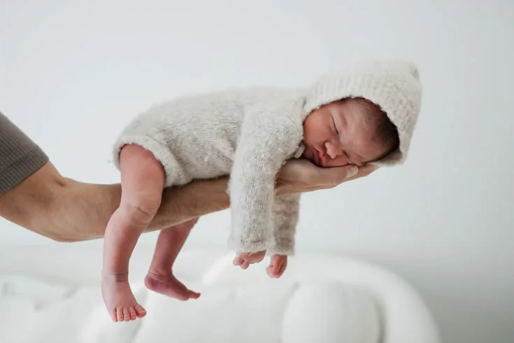 Sleeping newborn in a cream hood supported by an adult hand