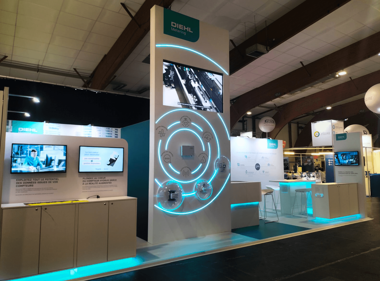 Stand Diehl Metering Carrefour de l'Eau 2026 réalisé par Expace – vue d'ensemble avec roue infographique rétroéclairée, médaillon végétal Empower a Sustainable Future, rétroéclairage cyan et comptoir Altair V5