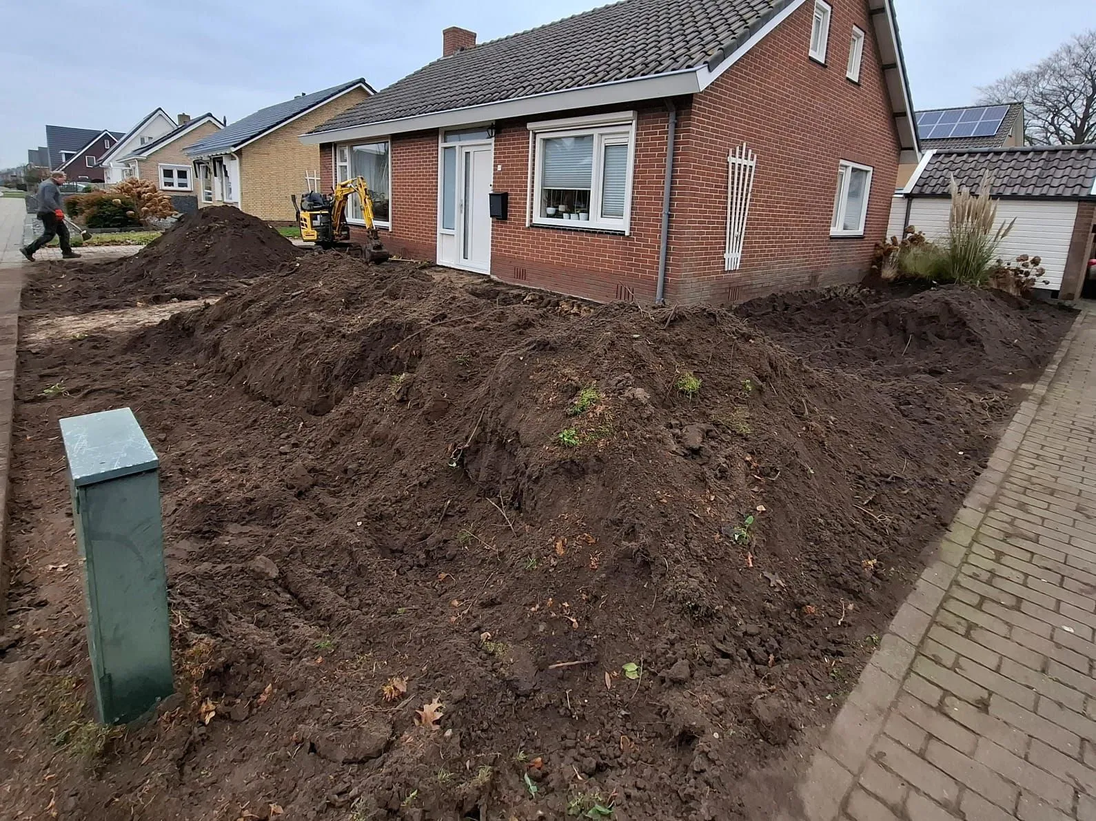 Voortuin in Harkema in renovatie met afgegraven grond en kleine graafmachine naast een vrijstaande woning.