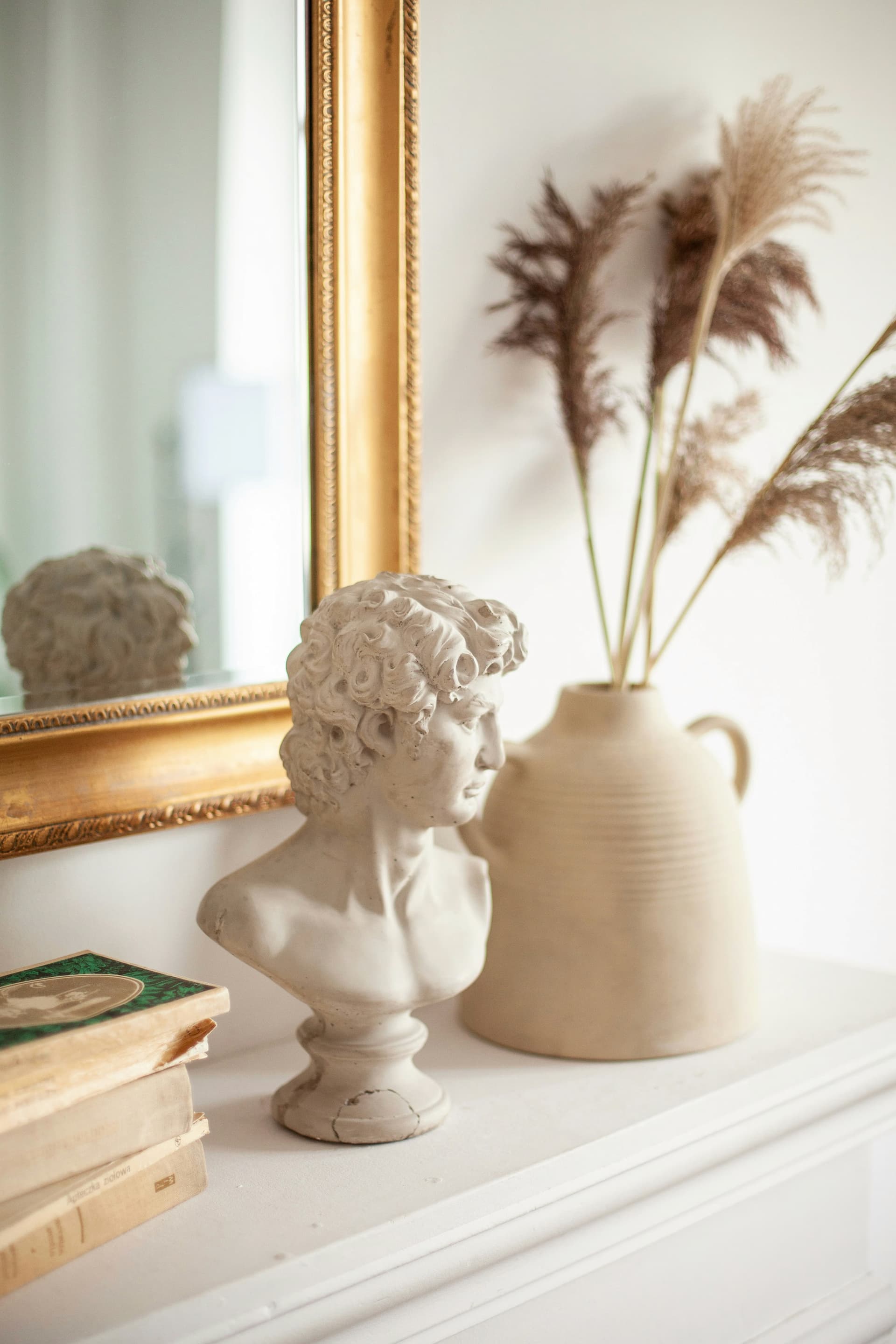A bust of a man on a shelf, accompanied by books and a mirror, creating an intellectual and reflective atmosphere.