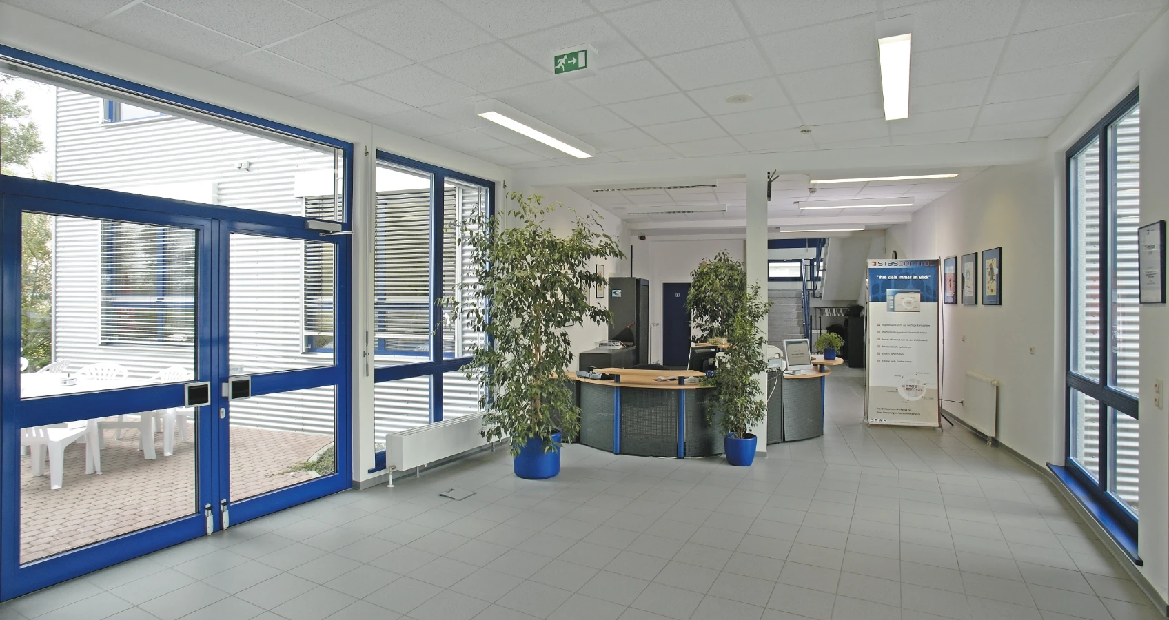 Empfangsbereich eines modernen Bürogebäudes mit großen Fenstern, Pflanzen und einem Schreibtisch.