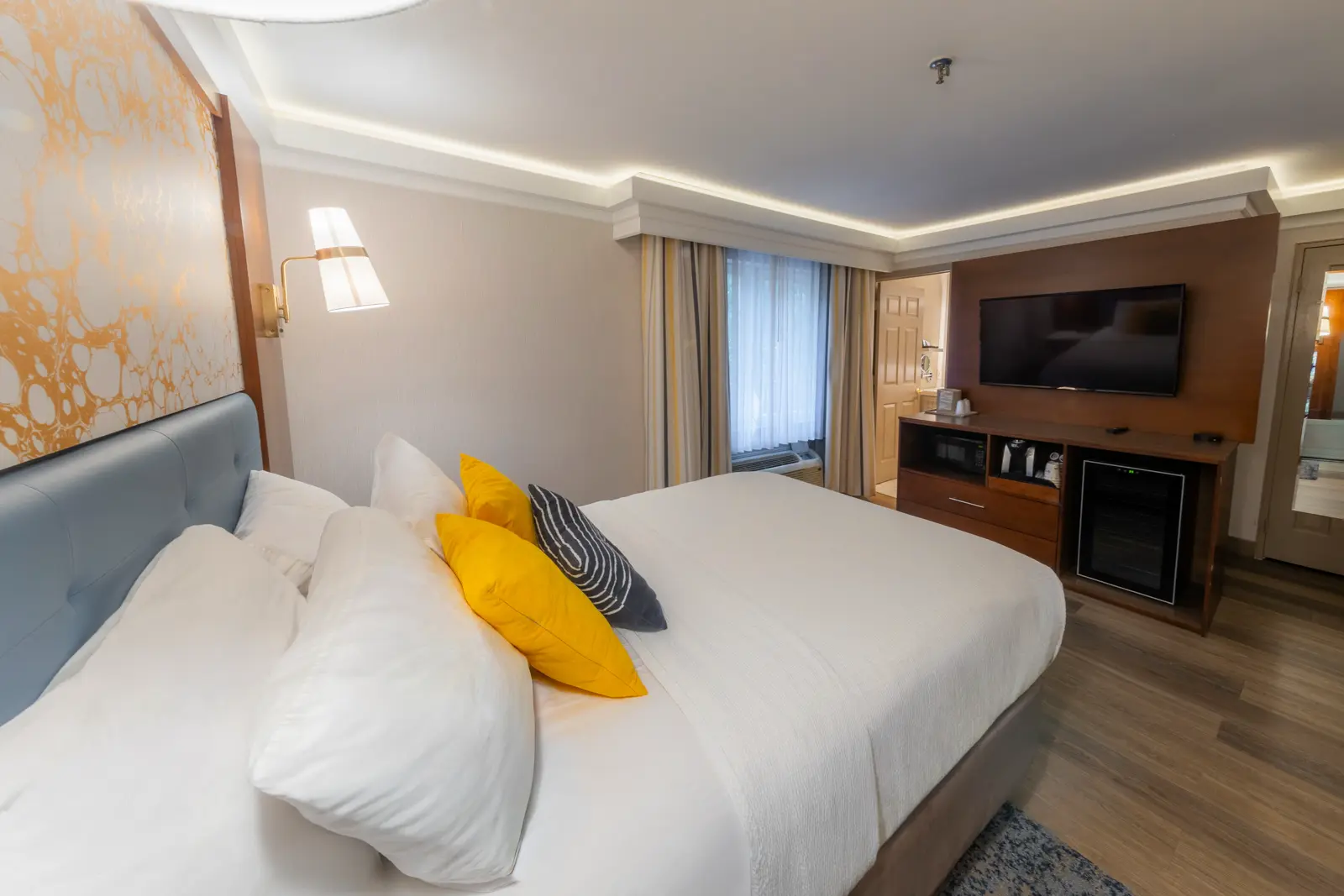 Three white pillows on a bed with a blue headboard and abstract gold wall art.