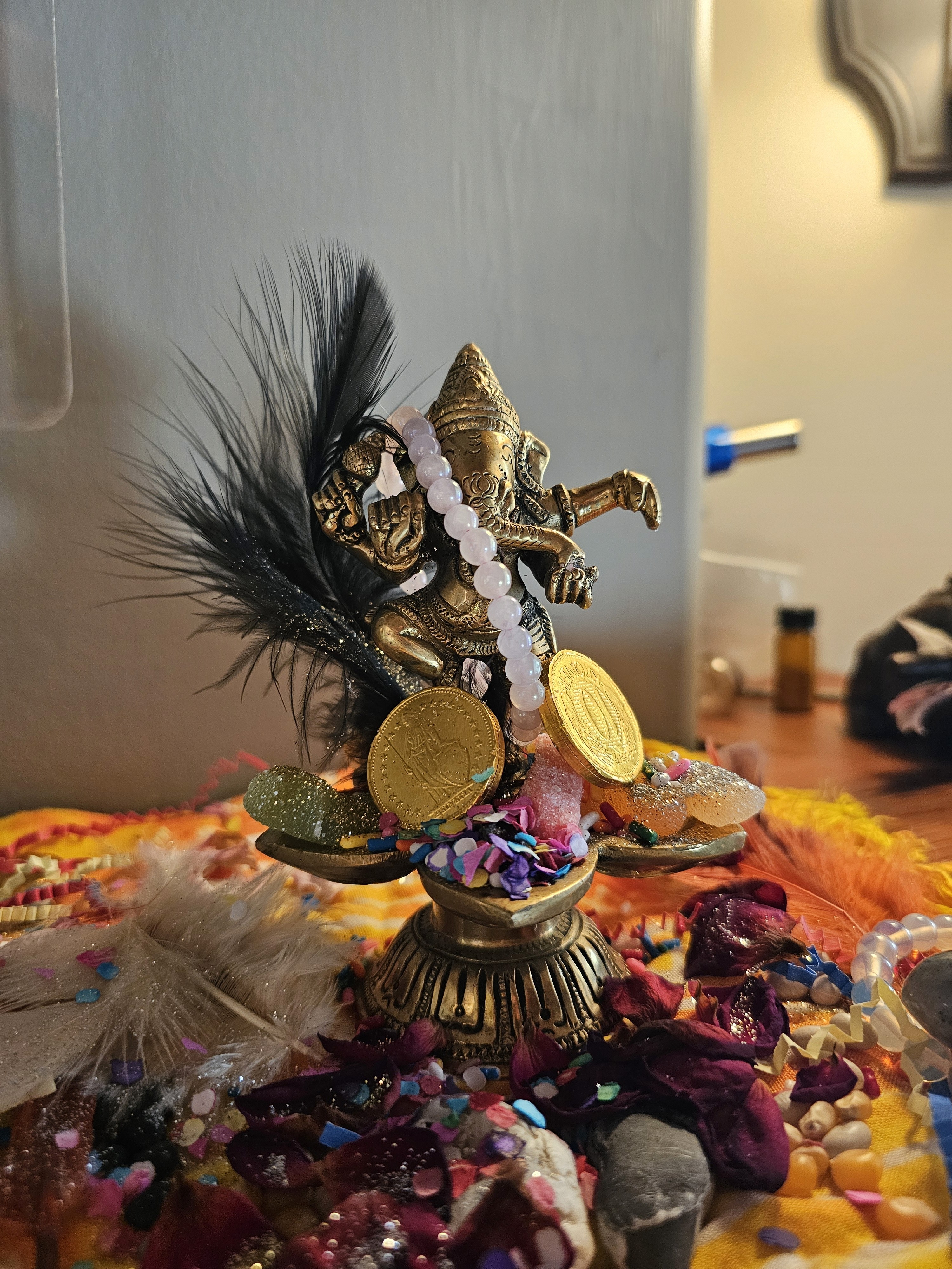 Sacred ceremonial altar featuring a Ganesha statue adorned with feathers, malas, gold coins, and colorful offerings