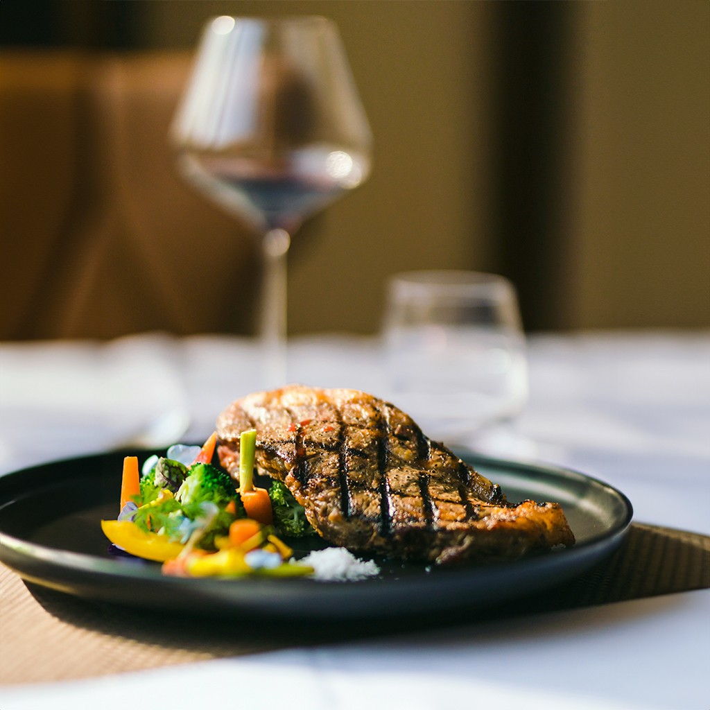 Nahaufnahme eines gegrillten Steaks mit Gemüse und einem Glas Rotwein im Restaurant Luna am Grün