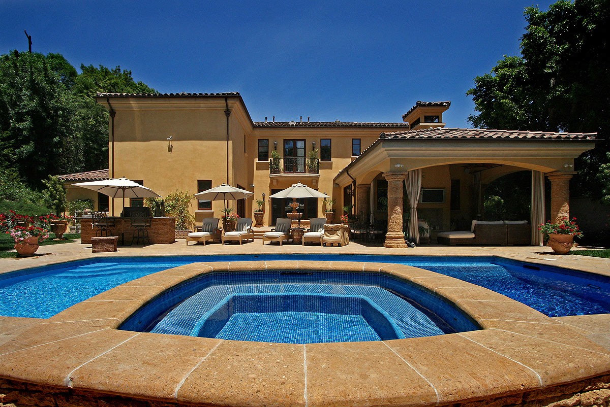 Close-up of the pool with the house in the background, under a clear blue sky, showcasing the luxurious setting.