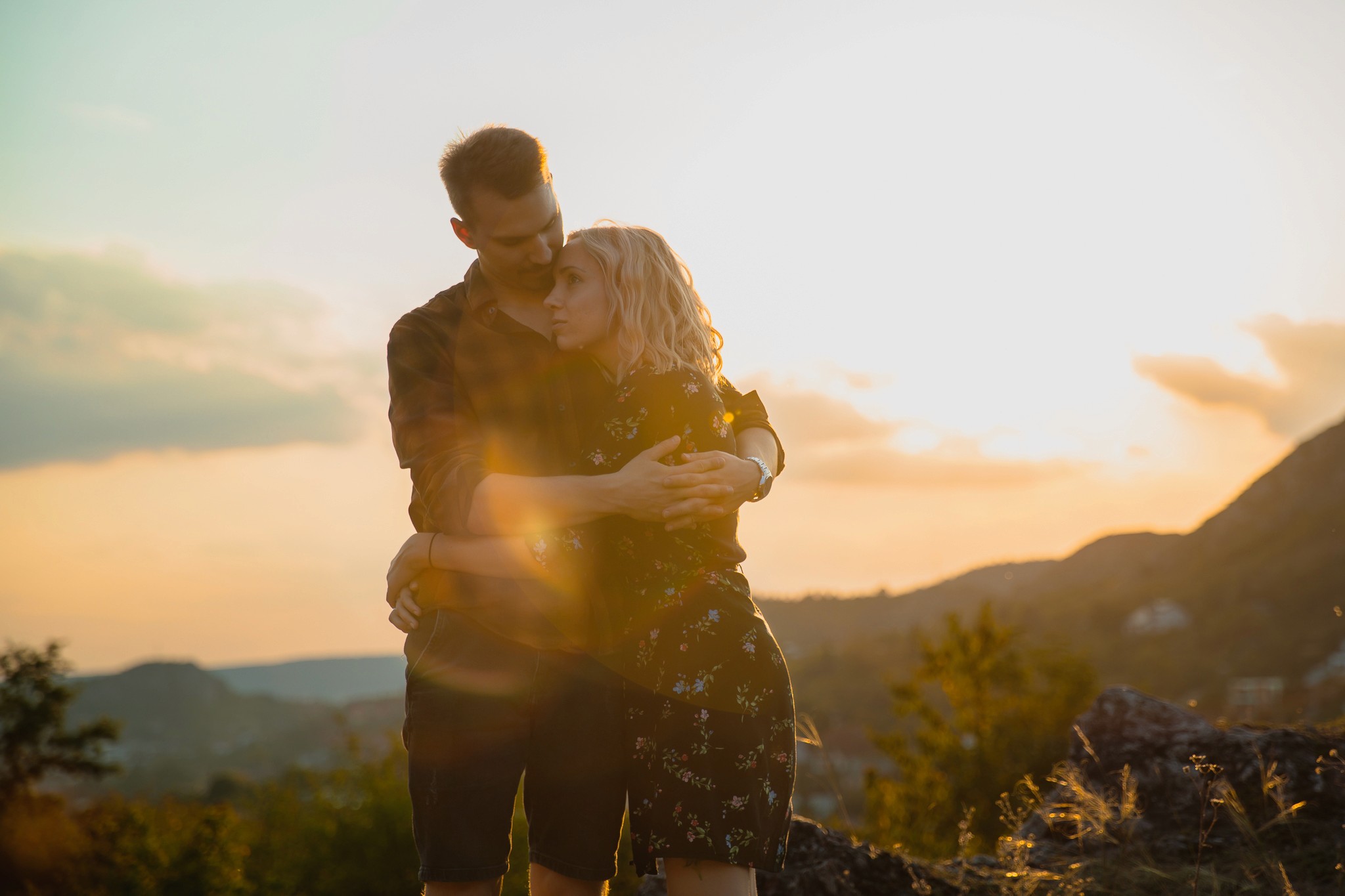 Fiatal pár sziklás kilátón, a férfi hátulról átöleli a nőt.