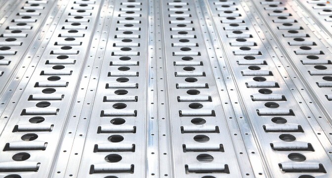 Close-up of a silver metal deck with repeating parallel slots and circular holes.
