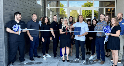 A group of people gathers for a ribbon-cutting ceremony outside a building, smiling and holding scissors.