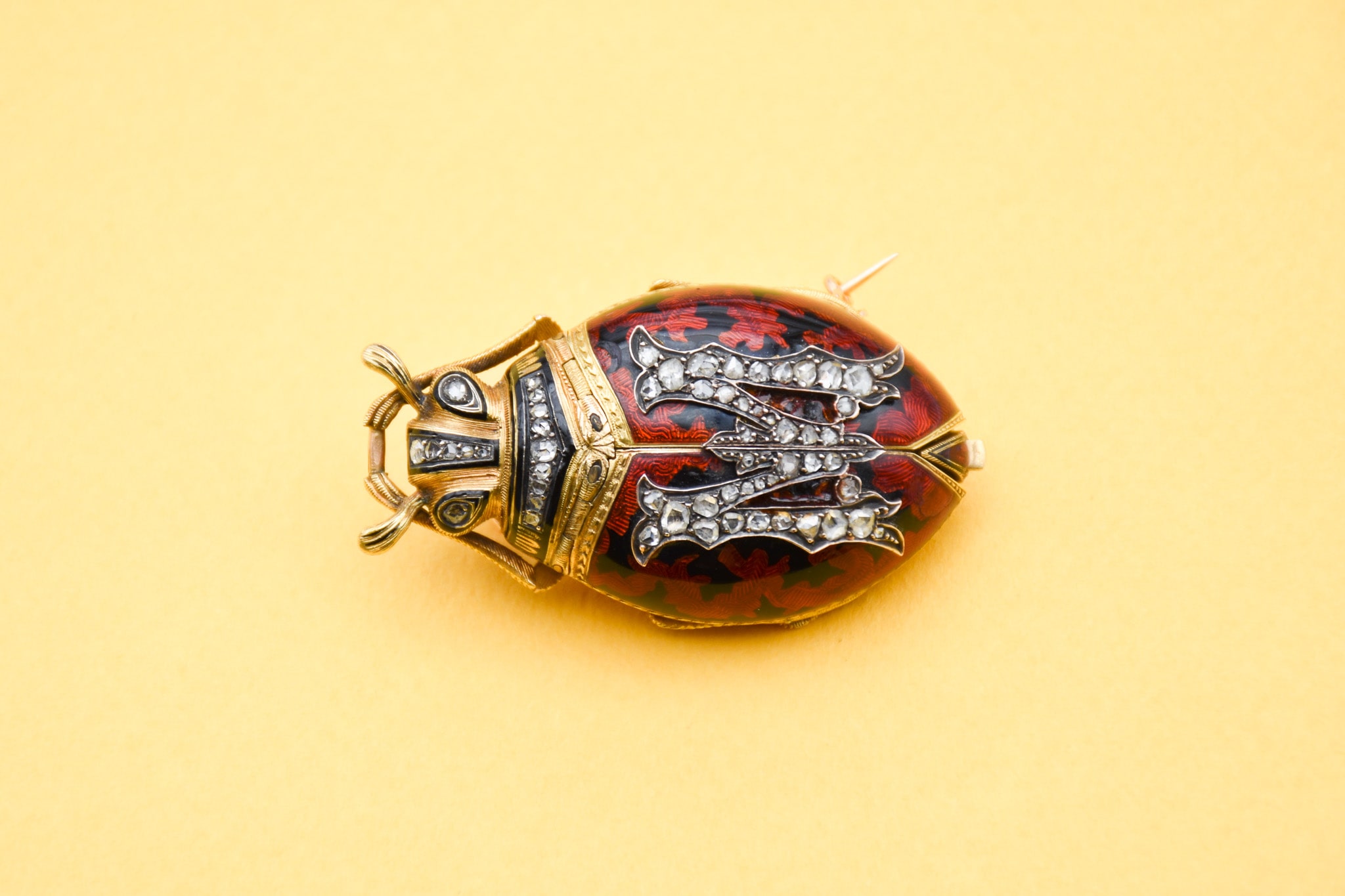 Broche Pendentif représentant une coccinelle aux ailes articulées dissimulant une montre à clé. Les ailes sont en émail rouges et noires et ornées de diamants formant la lettre M