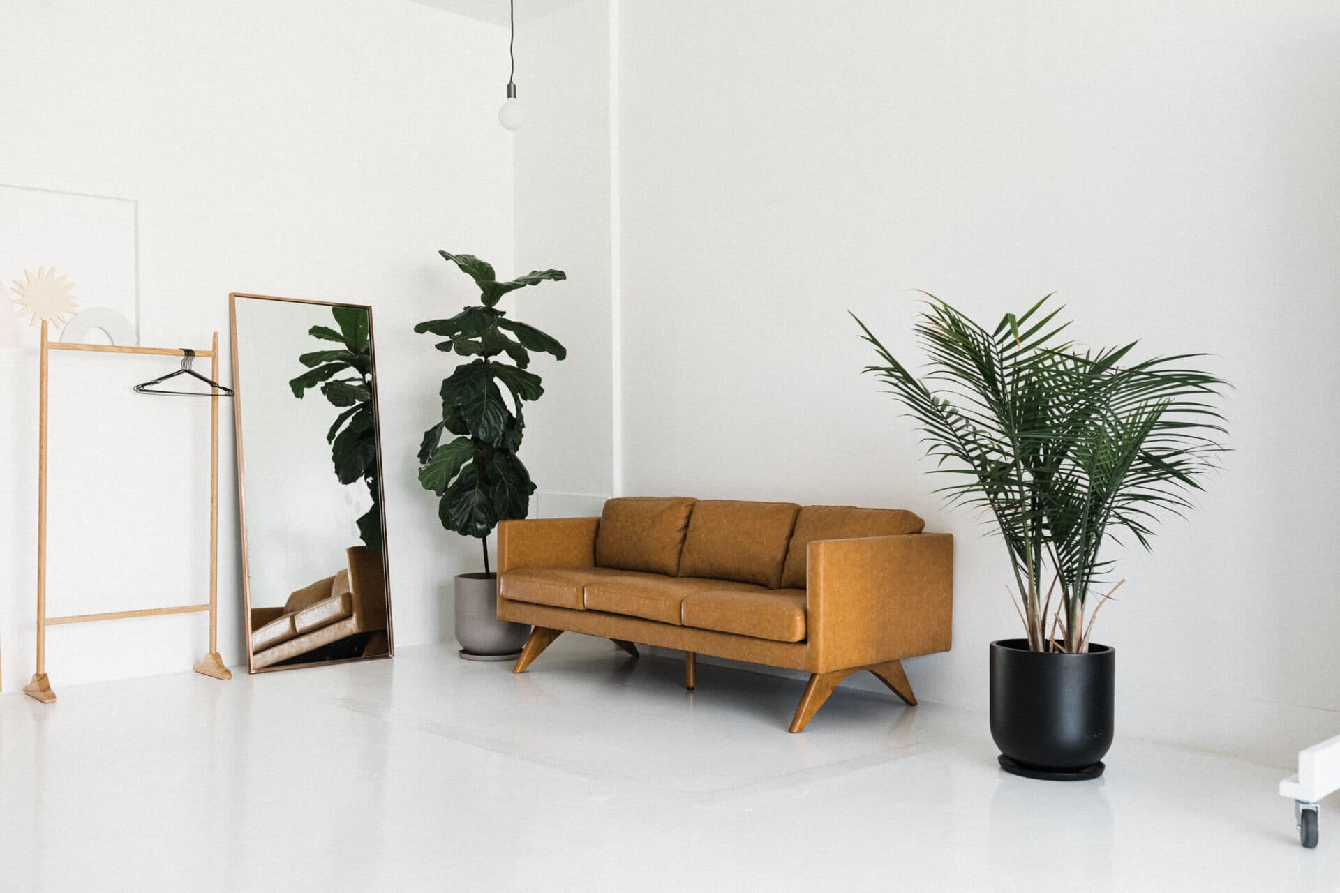 A bright and open space with a brown leather couch, plants, a mirror, and a clothing rack, capturing the natural light atmosphere at Revelator Studio, a photography studio in Shreveport