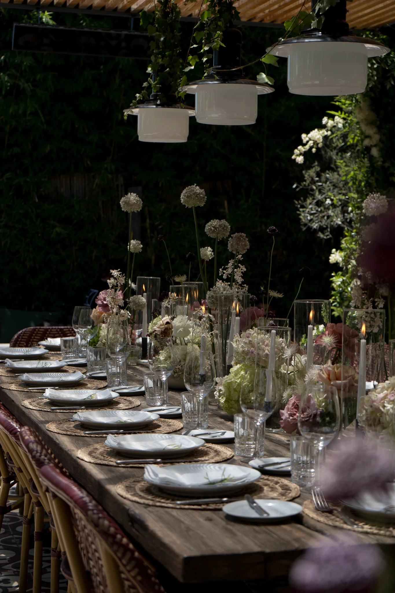 Perspectiva de mesa exterior con centros de mesa de hortensias, rosas y flores de tallo largo en ambiente relajado.