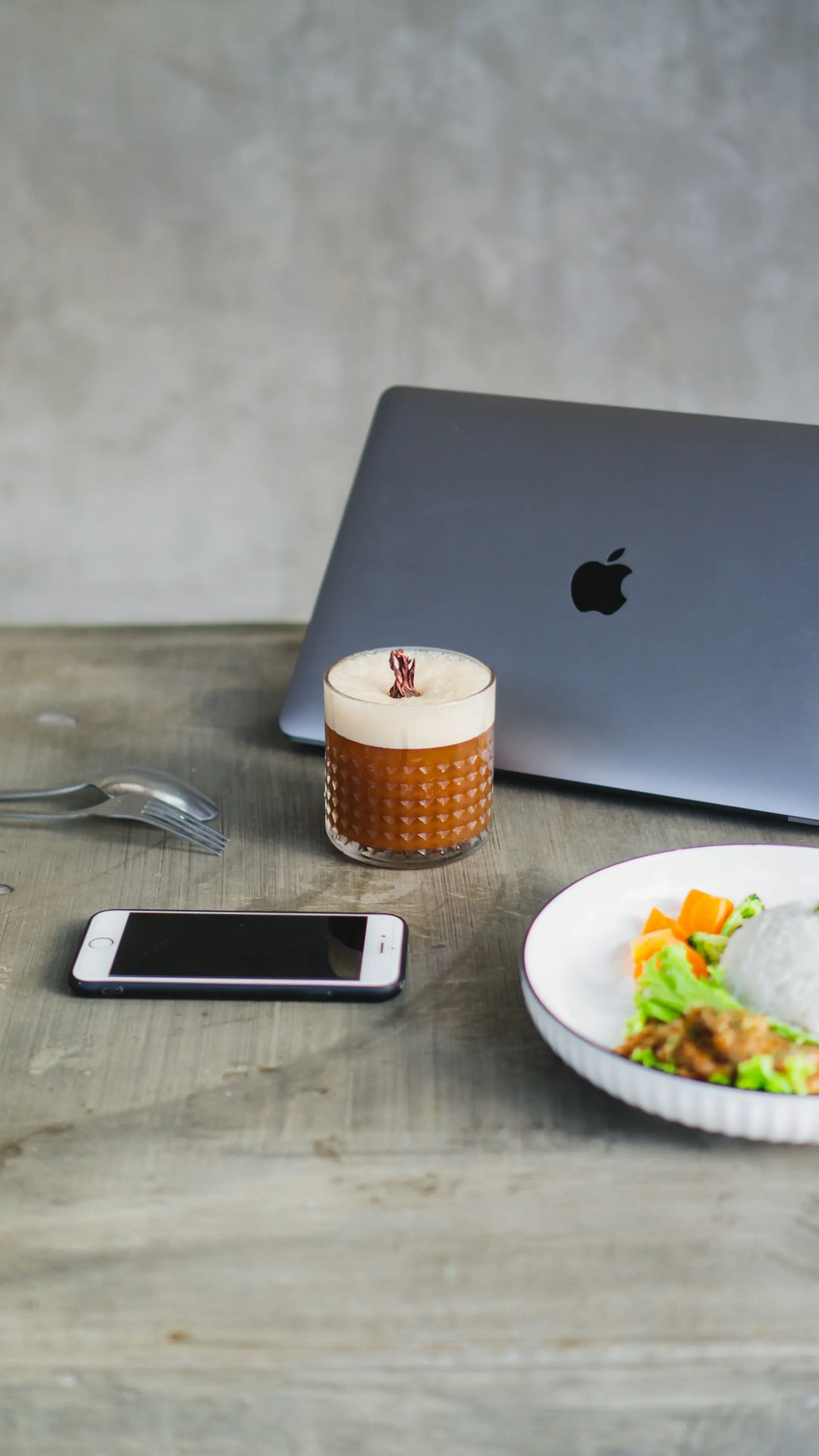 Cocktail glass with creamy foam placed on a table next to a laptop and smartphone, representing online restaurant browsing and digital reservations.